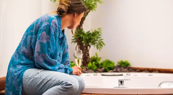 Mujer con copa de champán, disfrutando del slow living junto a una bañera y plantas.