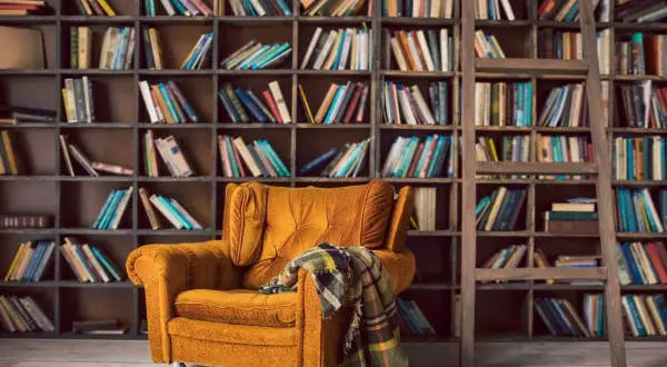 Un sillón acogedor y una manta a cuadros esperan en este rincón perfecto para un club del libro. Estanterías llenas de libros invitan a la lectura.