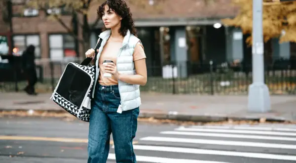 Mujer con bolso y café cruza la calle, lista para aplicar las 7 reglas para adelgazar caminando.