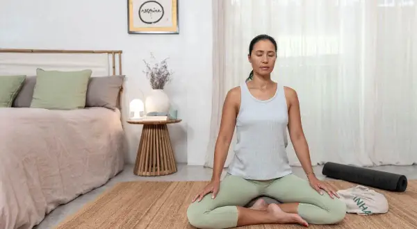 Mujer meditando en postura de loto, practicando mindfulness ejercicios en una habitación serena.