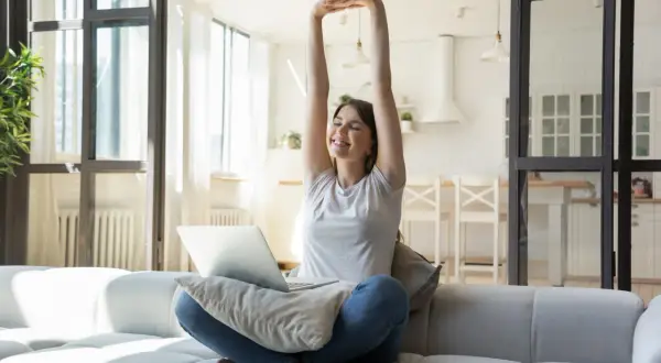 Joven estirándose en el sofá con un portátil, lista para cambiar su rutina y empezar el día con energía.