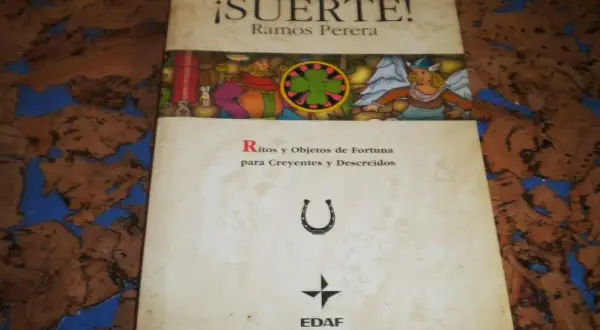 El libro de la buena suerte, "¡Suerte!" de Ramos Perera, explora ritos y objetos de fortuna. Incluye una herradura y un trébol.