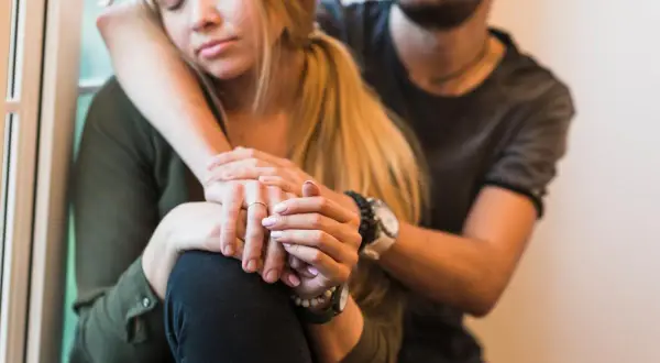 Una pareja se abraza, ella con los ojos cerrados y él consolándola, transmitiendo un profundo miedo al abandono.