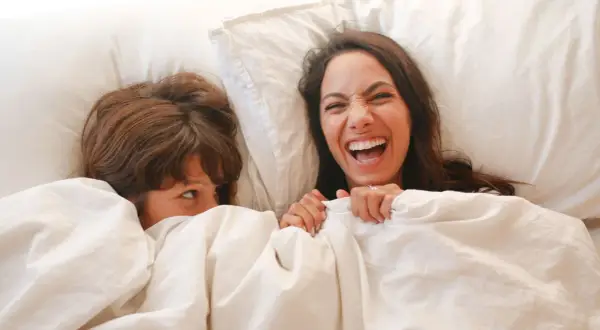 Dos personas riendo bajo las sábanas. Una pregunta que es ser asexual, es una forma de amar sin necesidad de contacto físico.