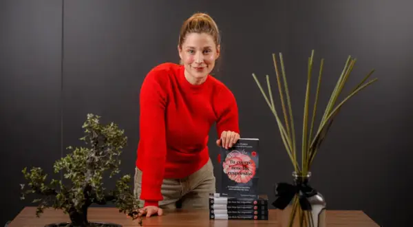 Mujer sonriente con suéter rojo, sosteniendo un libro sobre el cuerpo y la digestión, promoviendo el body positive.