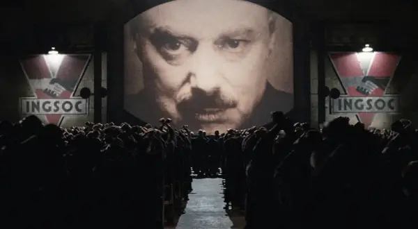 Multitud ante pantalla gigante con el rostro de un hombre y el logo de INGSOC. Un eco de las **1984 frases** que controlan sus mentes.