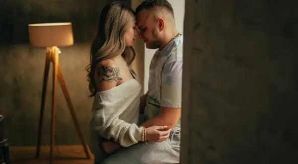 Una pareja se abraza tiernamente, sus frentes juntas. Ella tiene un tatuaje de flor en el hombro. Esto es hacer el amor de verdad: conexión y ternura.