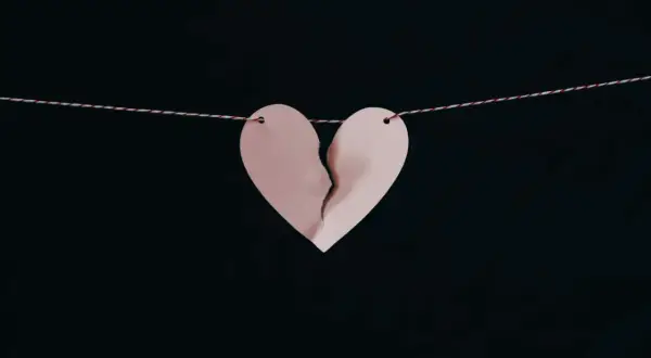 Corazón de papel rosa roto, colgado de un hilo, simbolizando los síntomas del desenamoramiento.