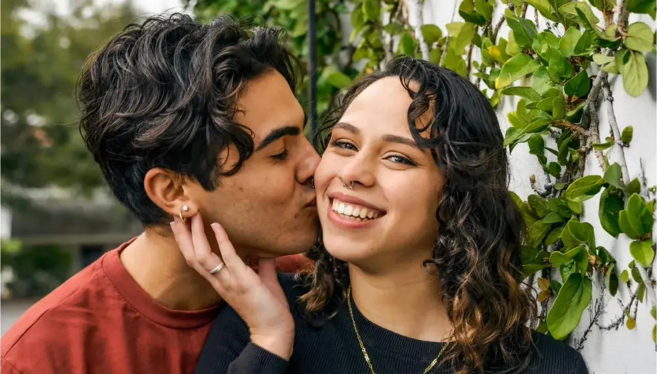 Un hombre de alto valor besa tiernamente a su pareja, rodeados de vegetación.