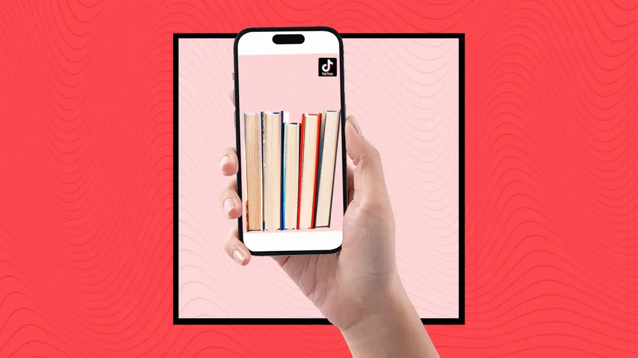Una mano sostiene un teléfono con libros en la pantalla, mostrando la comunidad de **que es booktok** y sus recomendaciones literarias.