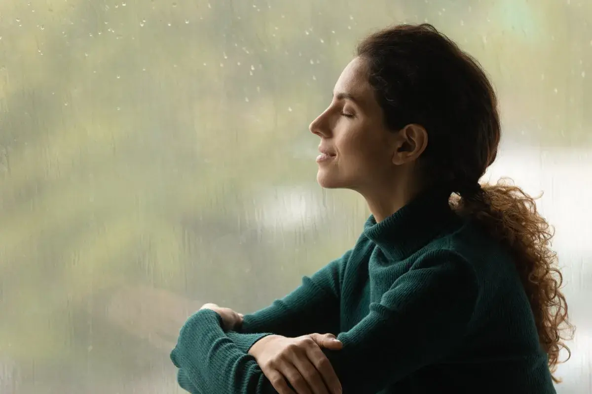 Mujer con los ojos cerrados, disfrutando de la lluvia y la paz interior.