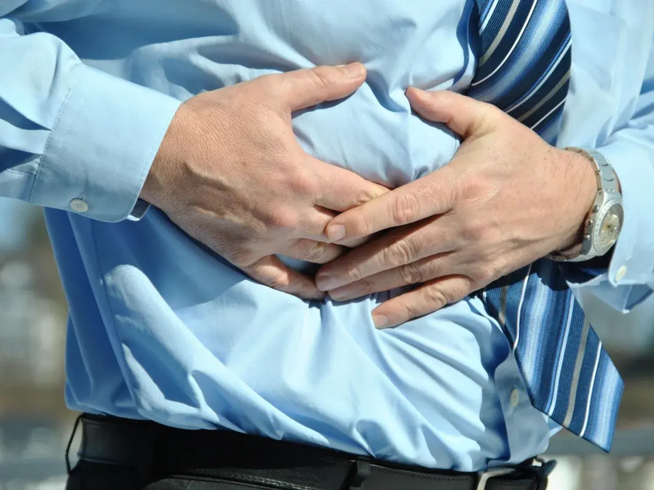 Hombre con camisa azul y corbata a rayas, sujetándose el abdomen por una **sensación de vacío en el estómago**.