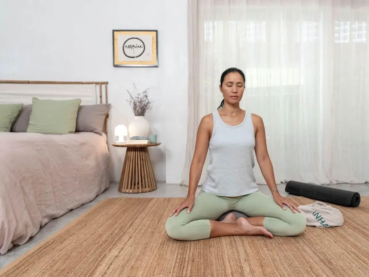 Mujer meditando en postura de loto, practicando mindfulness ejercicios en una habitación serena.