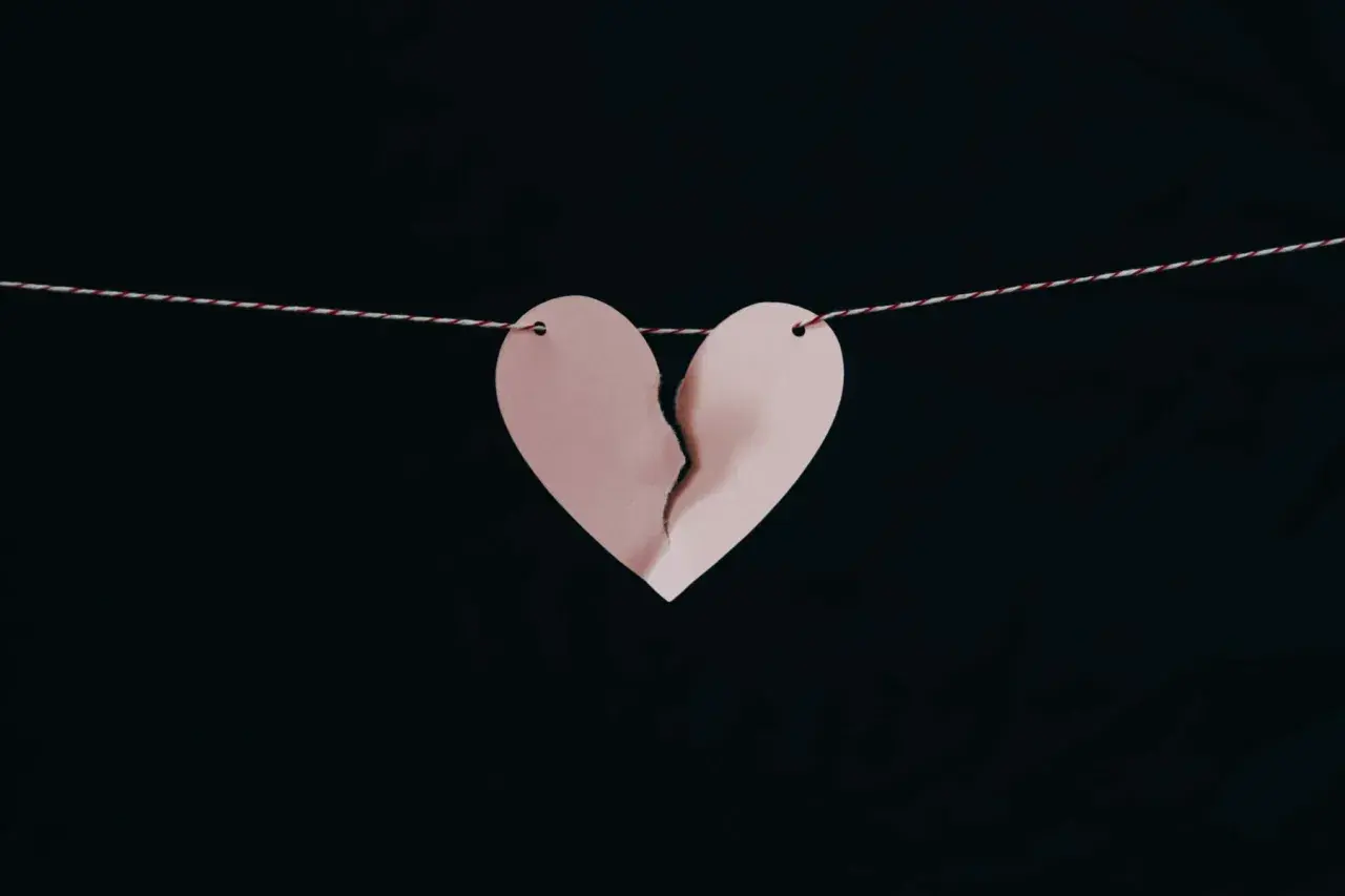 Corazón de papel rosa roto, colgado de un hilo, simbolizando los síntomas del desenamoramiento.