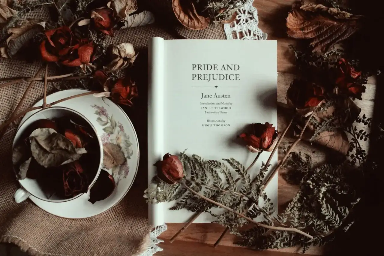 Un libro abierto de "Orgullo y Prejuicio" de Jane Austen, rodeado de rosas secas y helechos, evoca la atmósfera de sus obras.