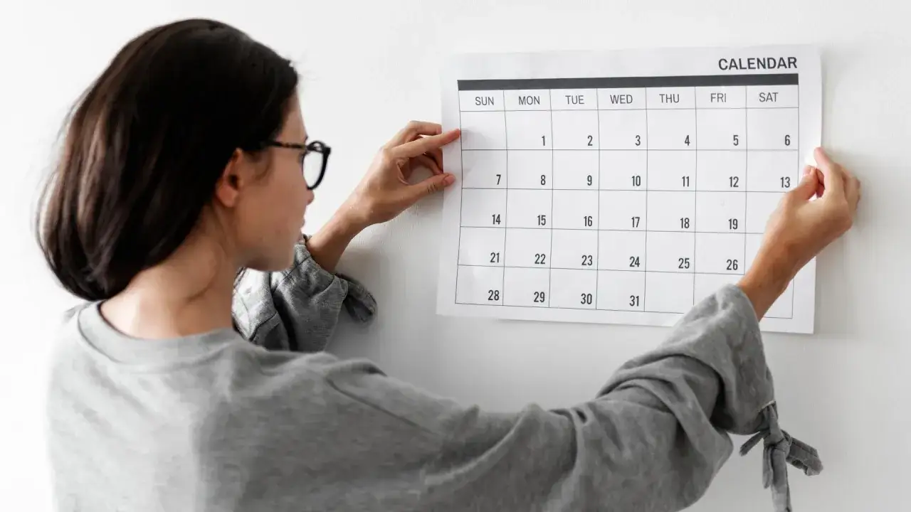 Mujer con gafas ajusta un calendario en la pared, planificando cómo tener disciplina para alcanzar sus metas.