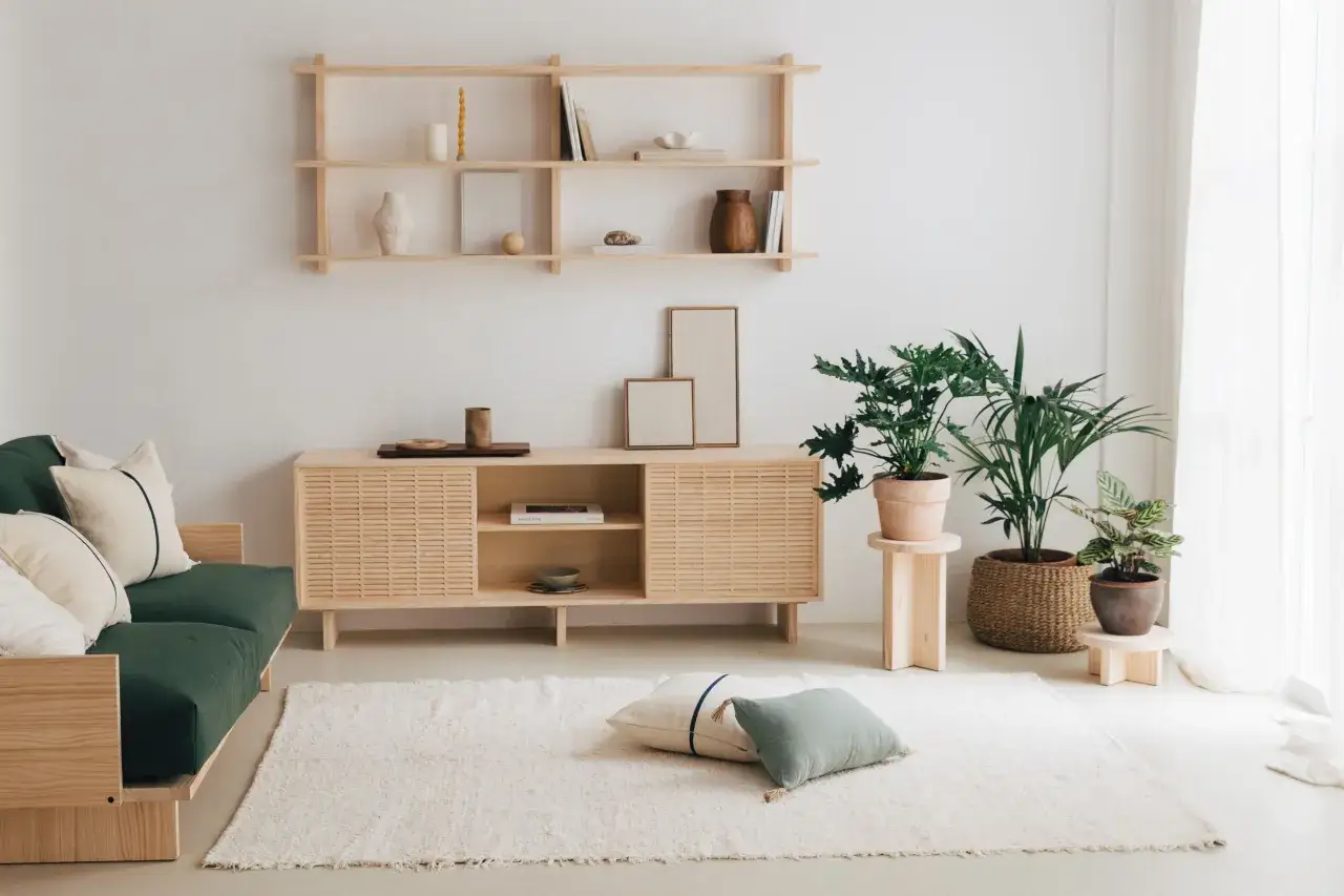 Un sal&oacute;n con sof&aacute; verde, mueble de madera y plantas, reflejando una vida minimalista.