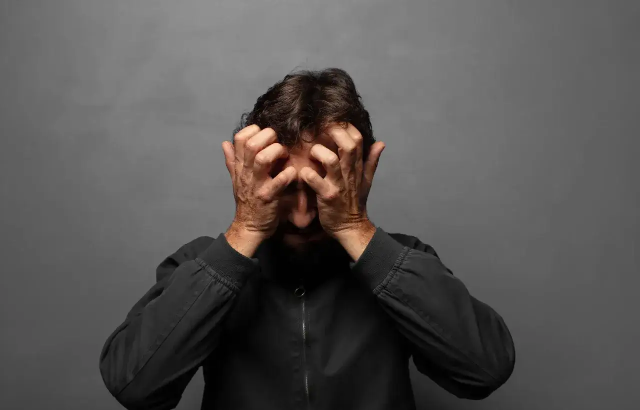 Hombre con las manos en la cabeza, rostro oculto, expresi&oacute;n de angustia que evoca una man&iacute;a persecutoria.