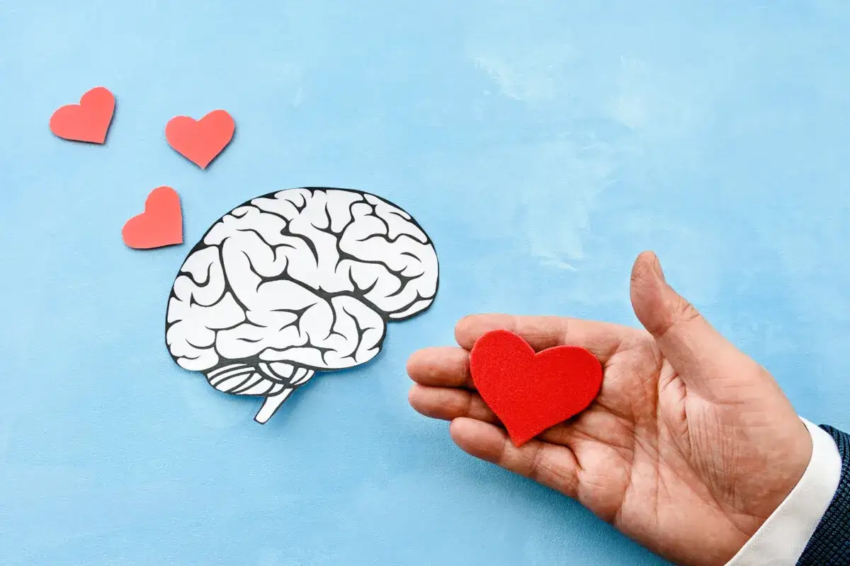 Un cerebro y corazones rojos flotan sobre un fondo azul. Una mano ofrece un coraz&oacute;n, ilustrando que es enamorarse.