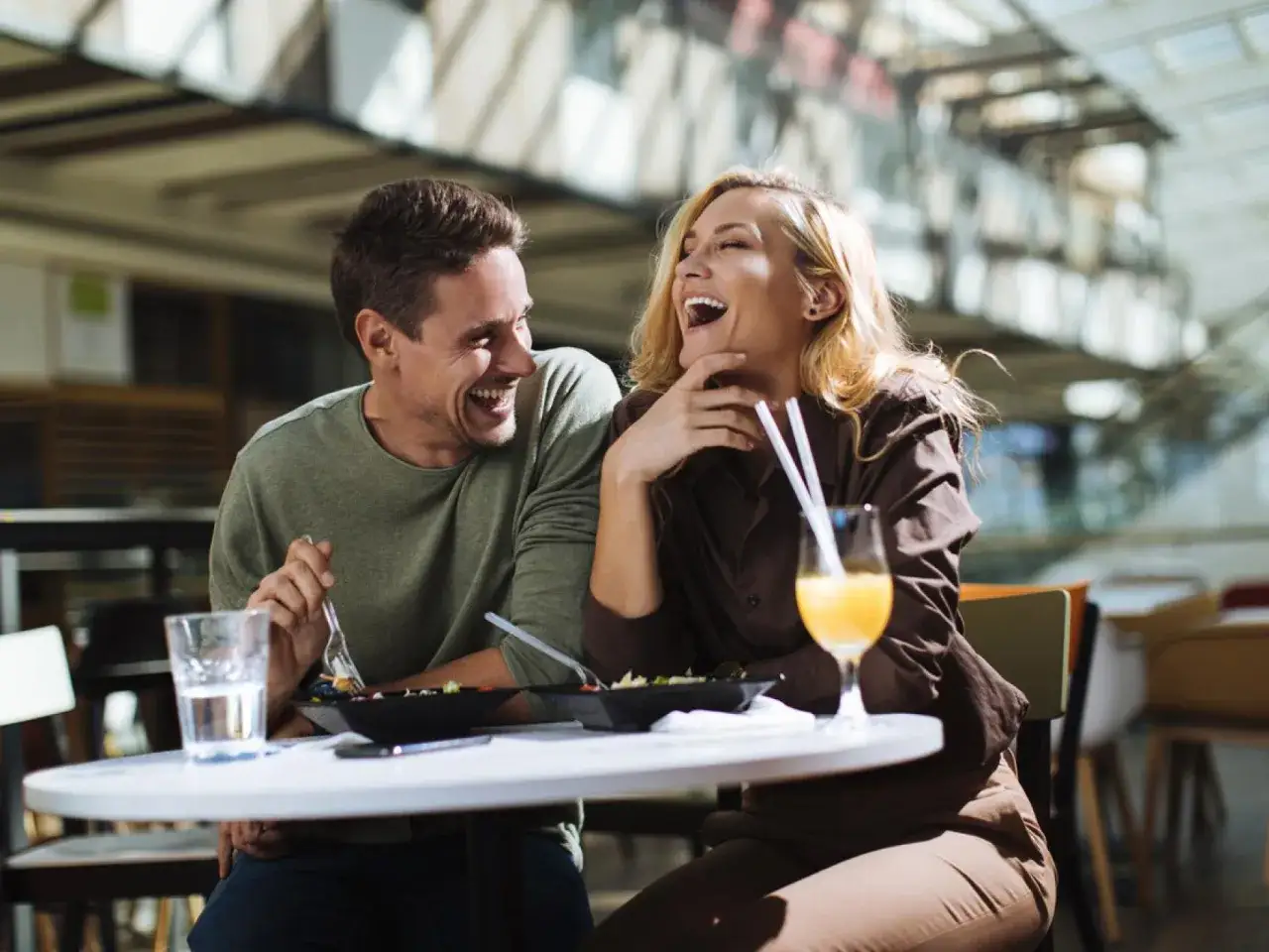 Pareja riendo en una cita, compartiendo comida y bebida. Una escena perfecta para aprender como enamorar a un hombre.