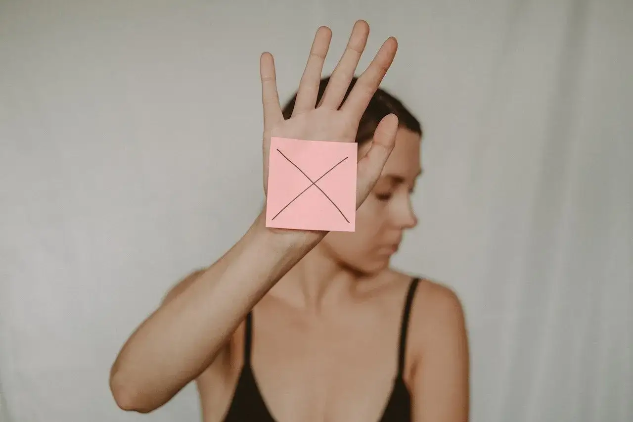 Mano con post-it rosa y una X dibujada, deteniendo la necesidad de ser el 