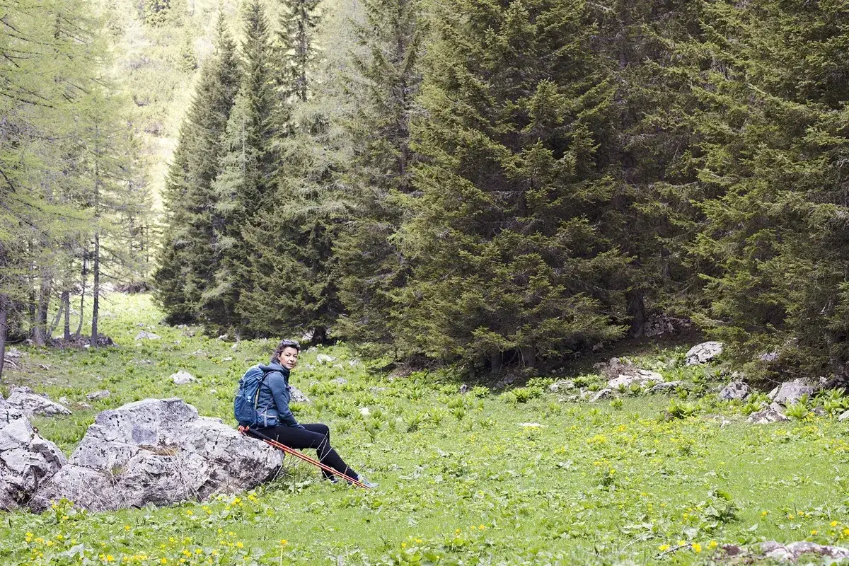 Mujer con mochila y bastones de senderismo sentada en una roca, disfrutando del paisaje. Un día perfecto para caminar 10 km diarios.