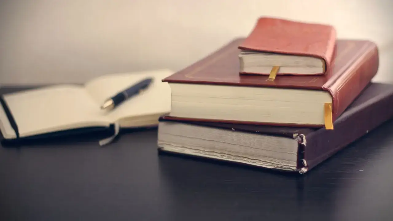 Pila de libros y un cuaderno abierto con un bolígrafo, listos para ser tus libros para aprender.