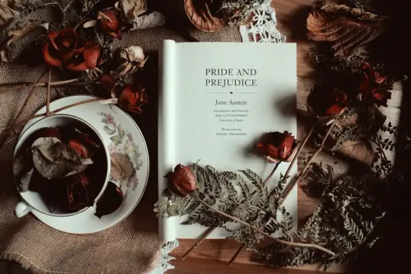 Un libro abierto de "Orgullo y Prejuicio" de Jane Austen, rodeado de rosas secas y helechos, evoca la atmósfera de sus obras.