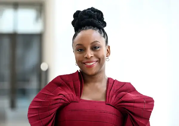 Chimamanda Ngozi Adichie, una de las escritoras famosas más influyentes, sonríe con un peinado recogido y un vestido rojo.