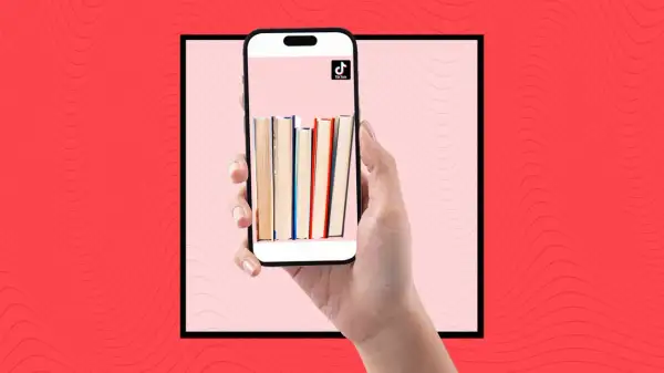 Una mano sostiene un teléfono con libros en la pantalla, mostrando la comunidad de **que es booktok** y sus recomendaciones literarias.