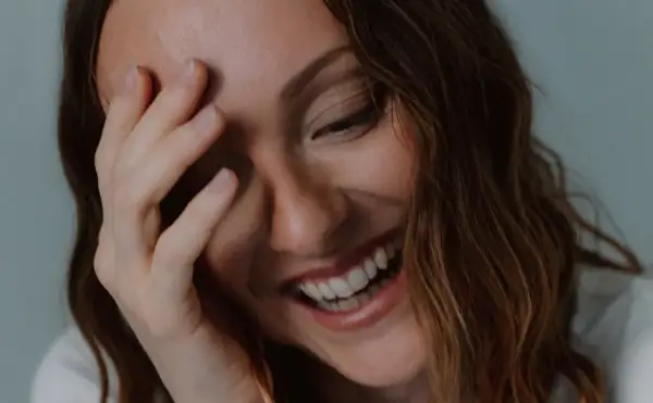 Una mujer ríe a carcajadas, cubriendo su rostro con la mano, un momento de pura labilidad emocional.