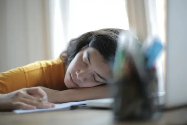 Joven con hipersomnia que es, duerme sobre sus brazos en un escritorio, con un lápiz en la mano.