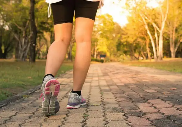 Piernas de una persona caminando por un sendero de adoquines en un parque, con el objetivo de caminar 10 km diarios.