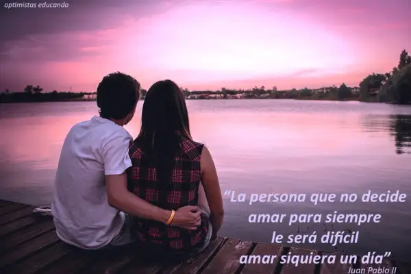 Pareja abraza en muelle al atardecer. La frase "existe el amor para toda la vida" inspira, sugiriendo que la decisión de amar siempre es clave.