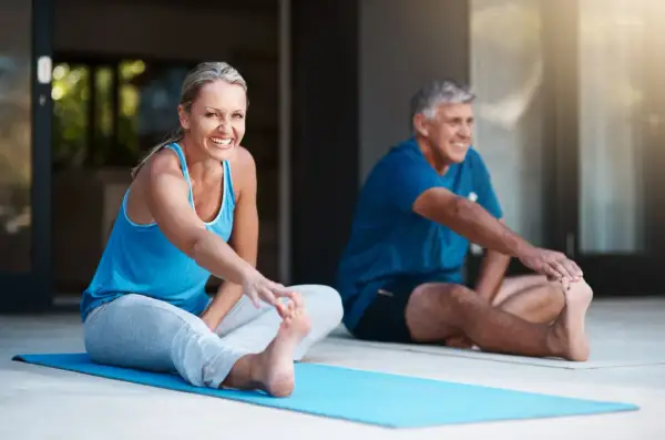 Pareja sonriente haciendo ejercicio en casa, estirando las piernas en una esterilla azul.
