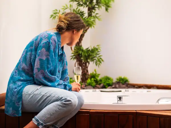 Mujer con copa de champán, disfrutando del slow living junto a una bañera y plantas.