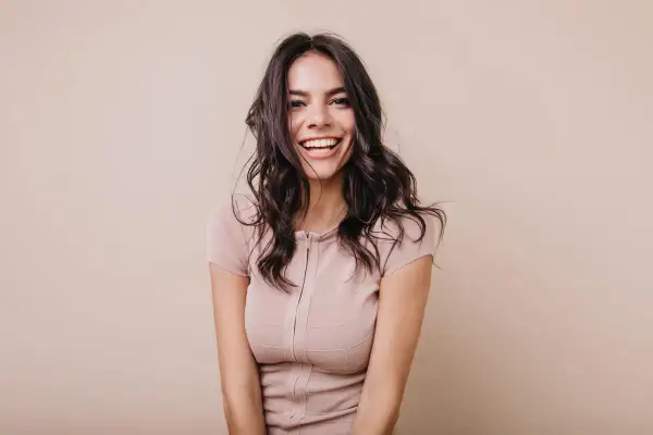 Mujer sonriendo con cabello oscuro y ondulado, luciendo un vestido beige. Su expresión irradia confianza, un ejemplo del "pretty privilege".