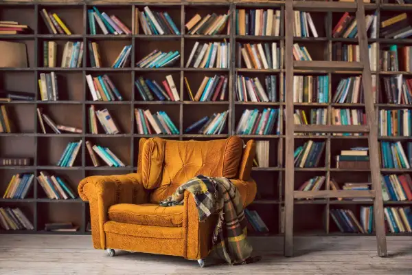 Un sillón acogedor y una manta a cuadros esperan en este rincón perfecto para un club del libro. Estanterías llenas de libros invitan a la lectura.