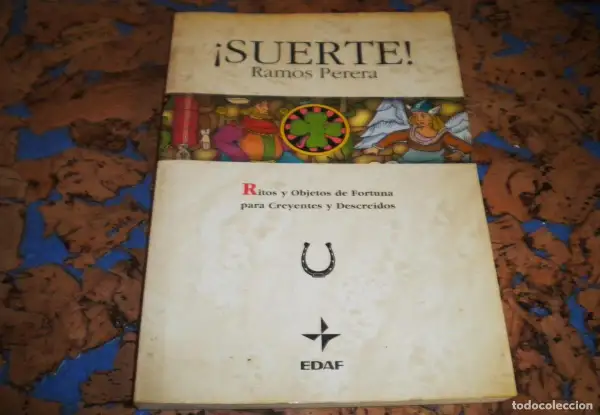 El libro de la buena suerte, "¡Suerte!" de Ramos Perera, explora ritos y objetos de fortuna. Incluye una herradura y un trébol.