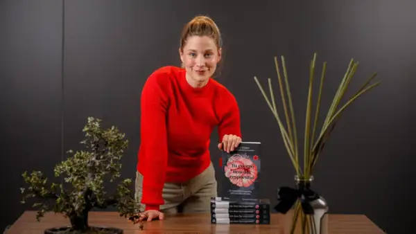 Mujer sonriente con suéter rojo, sosteniendo un libro sobre el cuerpo y la digestión, promoviendo el body positive.