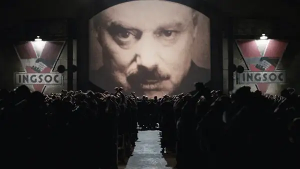 Multitud ante pantalla gigante con el rostro de un hombre y el logo de INGSOC. Un eco de las **1984 frases** que controlan sus mentes.
