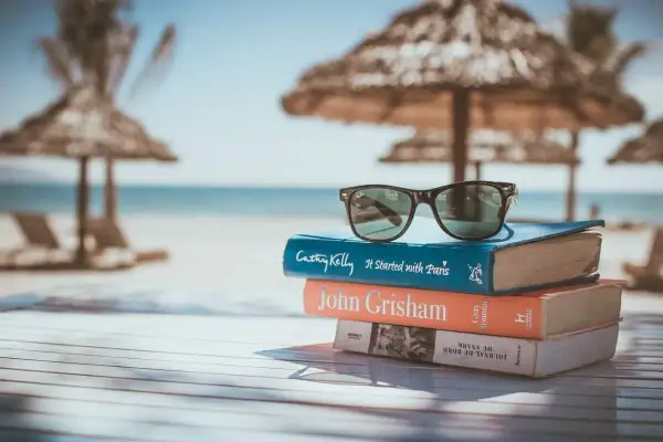 Gafas de sol sobre una pila de libros para leer en inglés, con la playa y el mar de fondo.