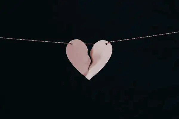 Corazón de papel rosa roto, colgado de un hilo, simbolizando los síntomas del desenamoramiento.