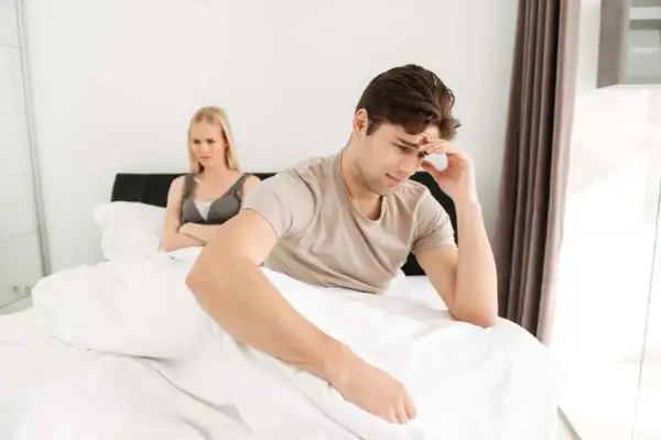 Pareja en cama, él pensativo, ella molesta. ¿Será que ella busca cómo enamorar a un hombre y él no se da cuenta?